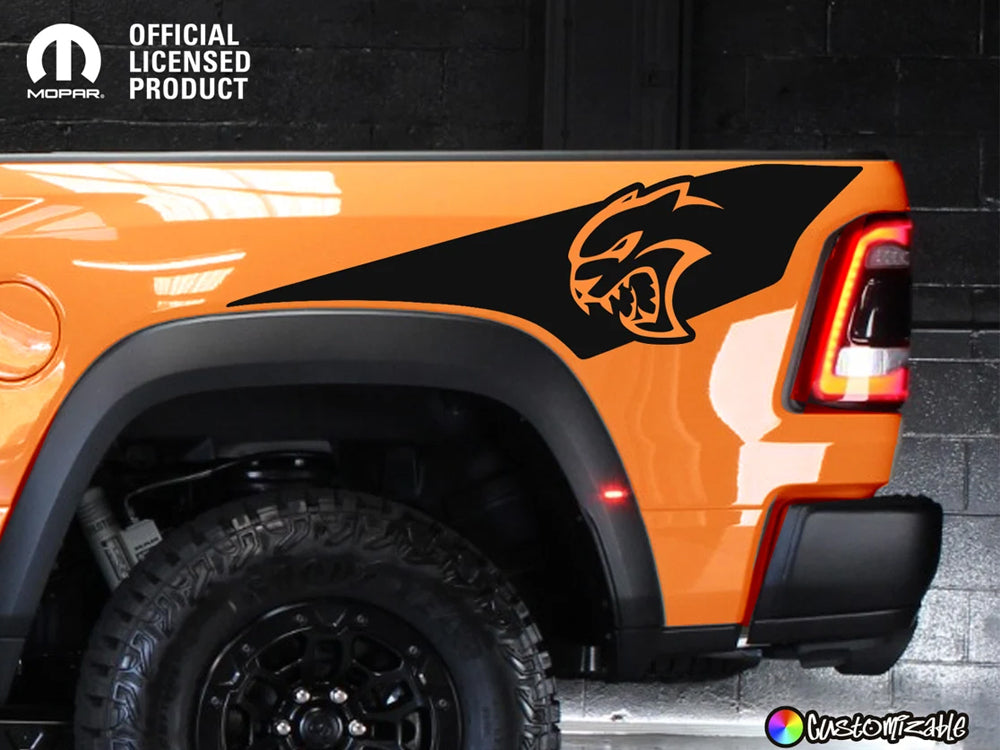 Orange RAM TRX truck with black Hellcat logo decal on bedside, showcasing custom Ignition Style graphics. Official licensed product by Mopar, displaying rugged off-road tires and sleek design against dark background.