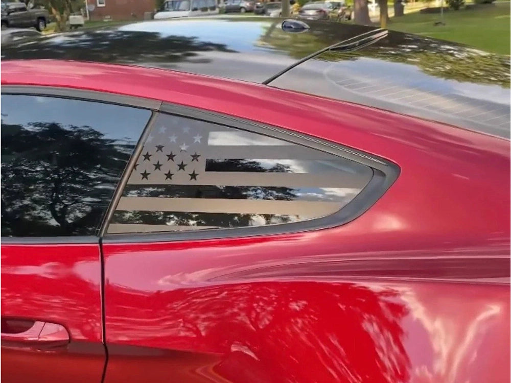 Red Ford Mustang with American flag decal on quarter window, showcasing custom vinyl design for S550 model. Tree reflections visible on shiny exterior.